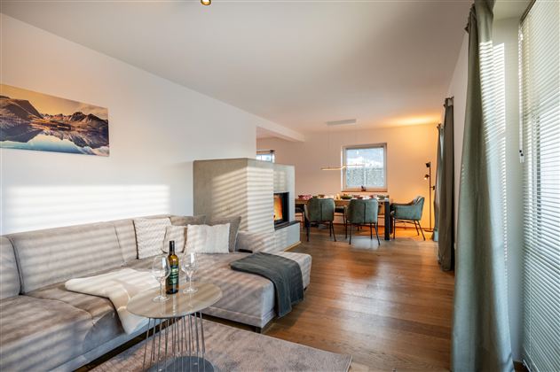 Ein modernes Wohnzimmer mit einem gemütlichen Sofa und einem Tisch. Der Raum ist hell und einladend, mit Blick auf einen Essbereich.