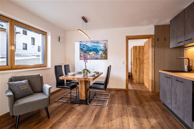 Een moderne woonruimte met een houten tafel en zwarte stoelen. De ruimte heeft grote ramen en een gezellige sfeer.