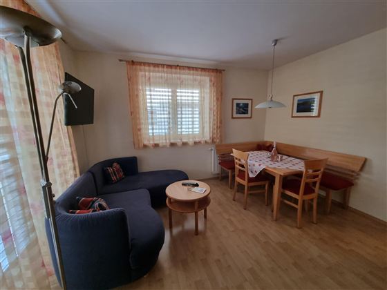 Een gezellige woonkamer met een donkerblauwe bank en een houten tafel. De ruimte is licht, met ramen die daglicht binnenlaten, en een eethoek.