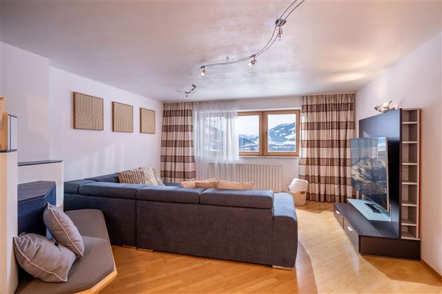 Ein modernes Wohnzimmer mit einem großen, dunklen Sofa. Vorhänge und Holzfußboden schaffen eine gemütliche Atmosphäre.