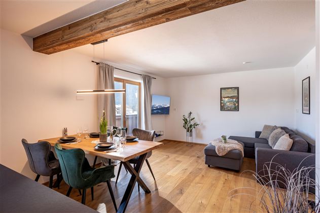 Een moderne woonkamer met een eettafel voor vier personen en elegante stoelen. Grote ramen zorgen voor veel daglicht en een gezellige sfeer.