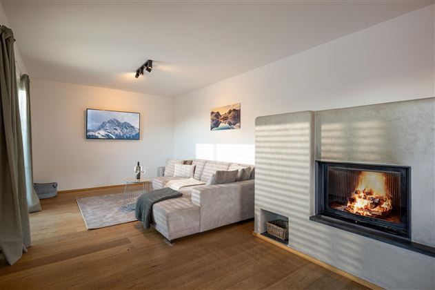 Ein modernes Wohnzimmer mit einer bequemen Couch und einem Kamin. Helle Farben und große Fenster sorgen für eine einladende Atmosphäre.