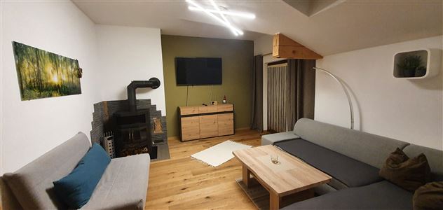 A modern living room with gray sofas and a wooden floor. The room is bright and cozy, with a TV and a decorative fireplace.