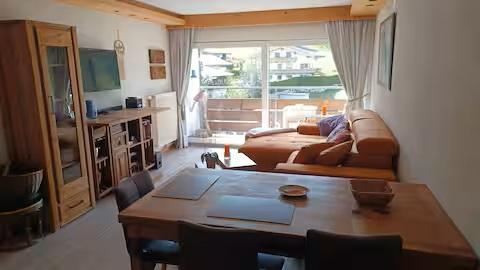 Een lichte woonkamer met een gezellige bank en een eettafel. Grote ramen bieden uitzicht op de omgeving en veel daglicht.