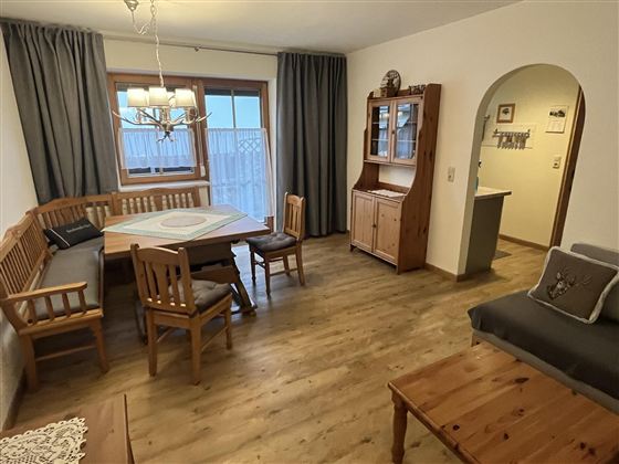 A cozy living space with wooden furniture and a dining table. Large windows provide plenty of light.