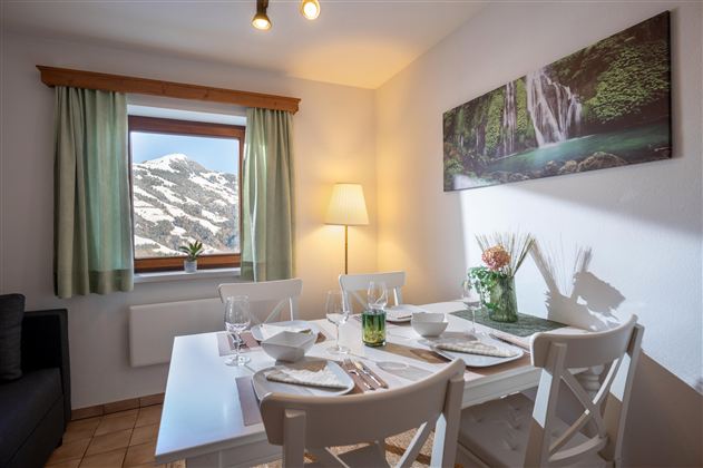 Ein helles Esszimmer mit weißem Tisch und dekorierten Plätzen. Durch das Fenster ist eine verschneite Berglandschaft sichtbar.