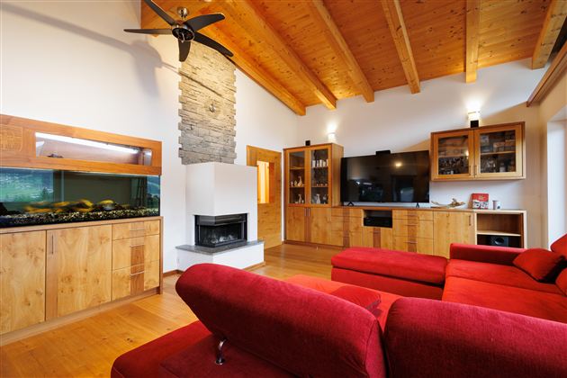 Ein modernes Wohnzimmer mit rotem Sofa und Holzwänden. Ein Aquarium, großer TV und ein Kamin verleihen dem Raum eine gemütliche Atmosphäre.