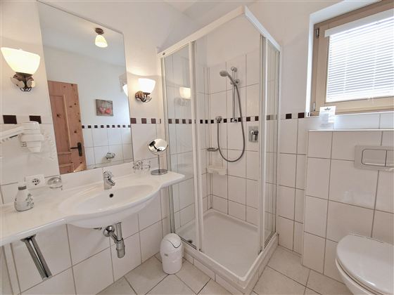 A modern bathroom with a shower, a sink, and a toilet. The walls are tiled with white tiles and there is a lot of natural light.
