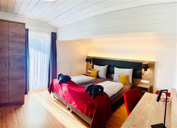 Een comfortabele slaapkamer met een groot tweepersoonsbed en gezellige kussens. De ruimte is licht en modern met een bureau en een kledingkast.