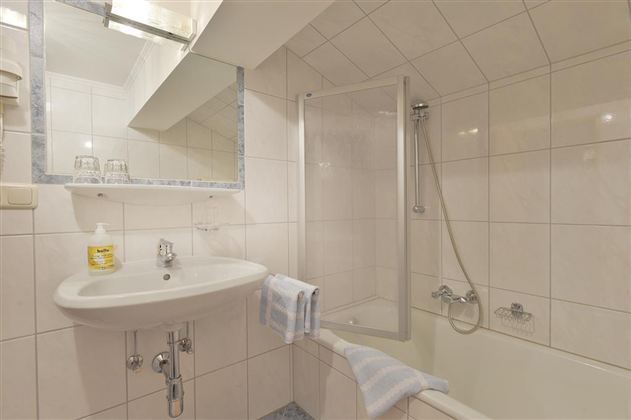 A modern bathroom with a bathtub and a shower. The walls are bright tiled, and there is a large mirror above the sink.