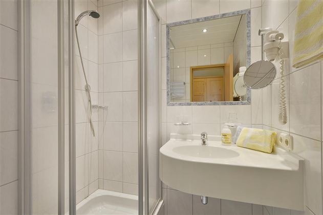 A modern bathroom with a shower and a sink. The walls are tiled in light colors, and a mirror reflects the space.