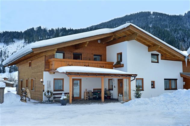 Ein modernes Haus mit Holz- und Putzfassade in einer verschneiten Landschaft. Im Hintergrund sind Berge zu sehen.